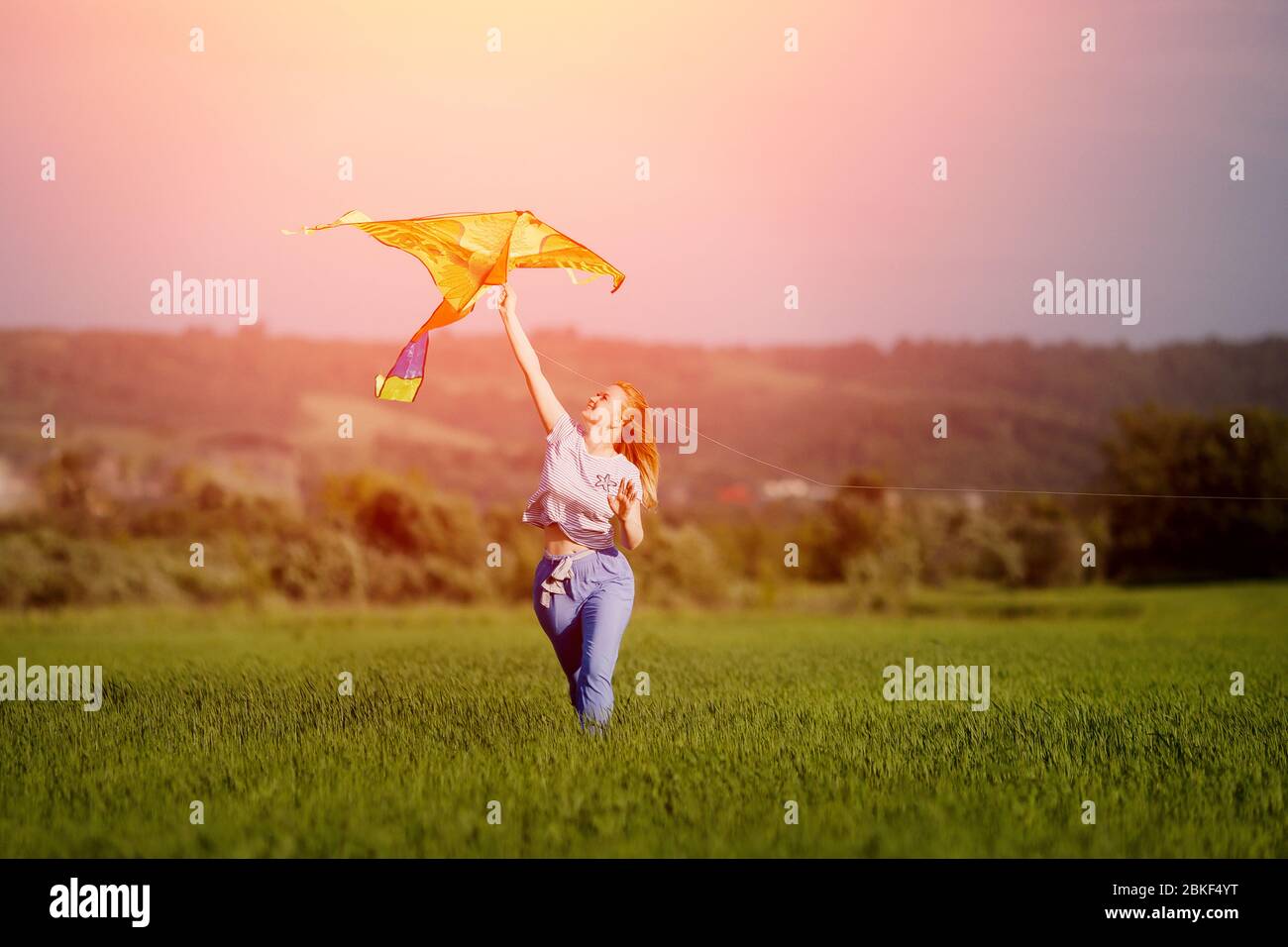 Young woman runs with kite through clean field at sunset, wind blows her hair. Concept of freedom from shackles, judgments. Stock Photo