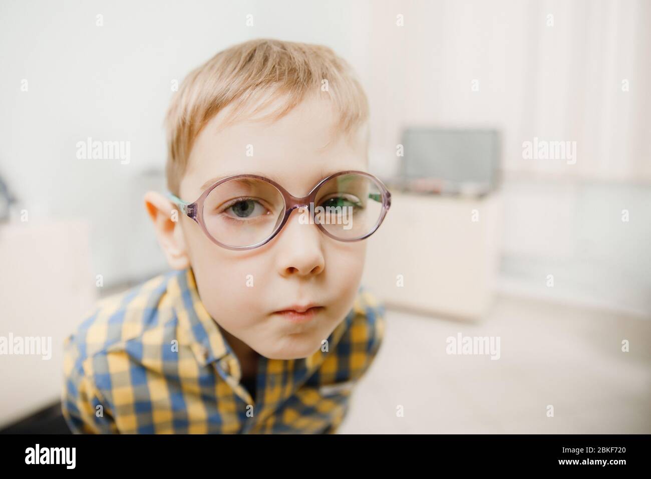 Child boy squints in glasses for eyes of sight, looks into frame. Concept reception ophthalmologist. Stock Photo