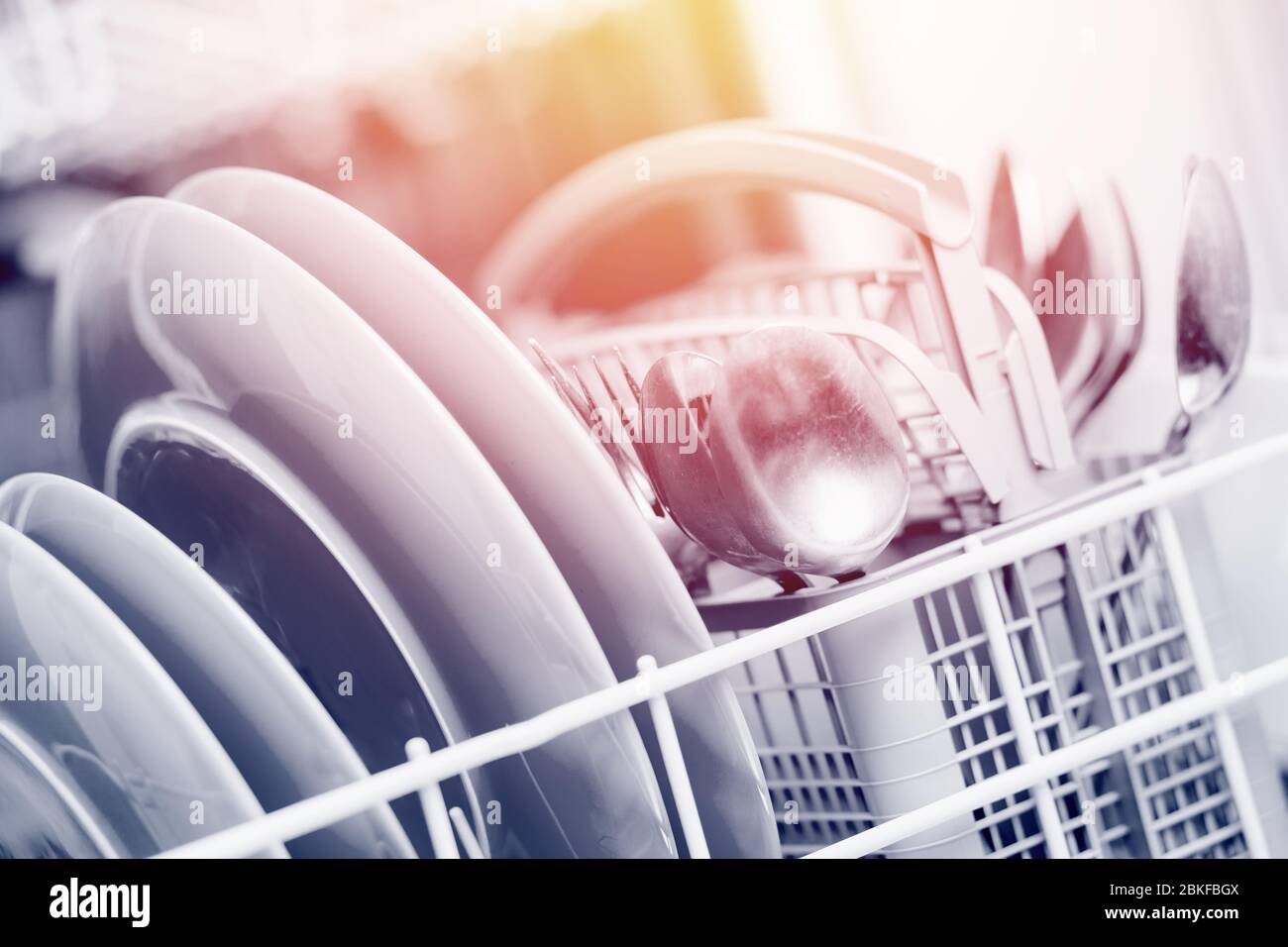 Open dishwasher with clean shine dishes and forks, spoons, cutlery