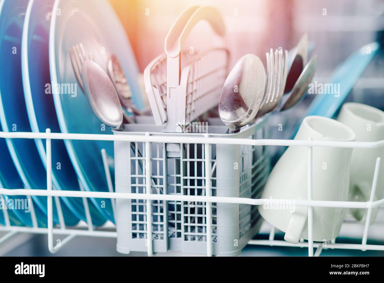 Open dishwasher with clean shine dishes and forks, spoons, cutlery