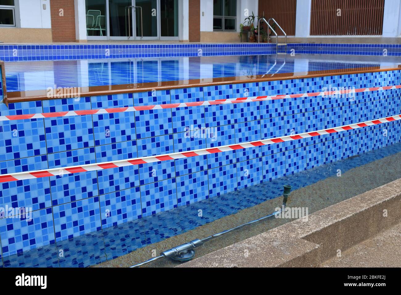 Barricade tape surrounding swimming pool, people do not allow to swim, they have to keep physical distancing due to coronavirus pandemic Stock Photo
