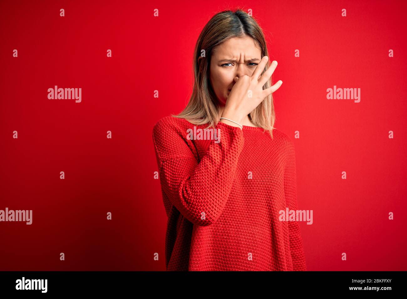 Young beautiful blonde woman wearing casual sweater over red isolated ...