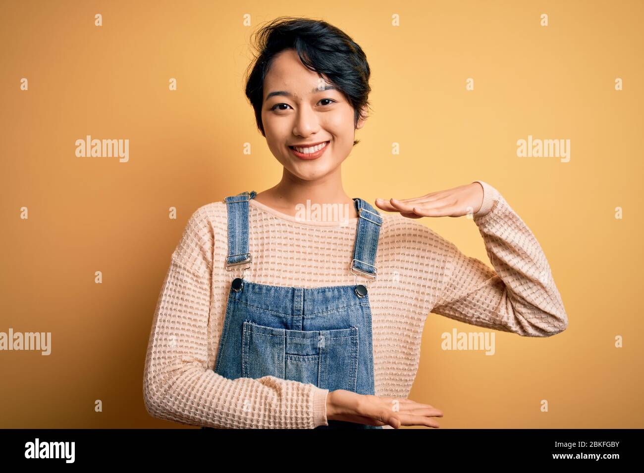 Young beautiful asian girl wearing casual denim overalls over isolated ...