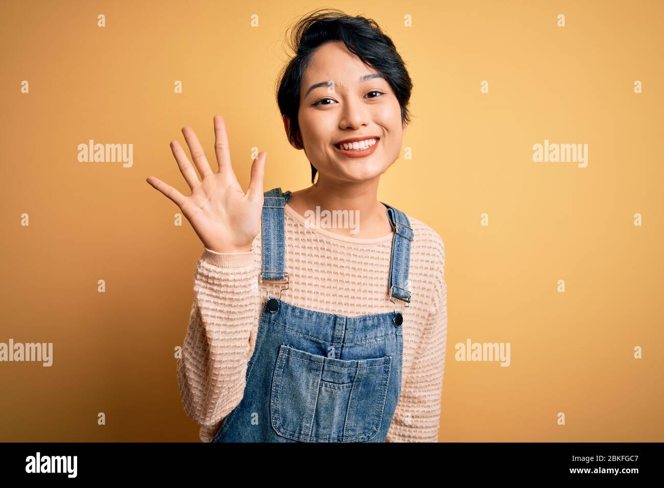 Young beautiful asian girl wearing casual denim overalls over isolated ...
