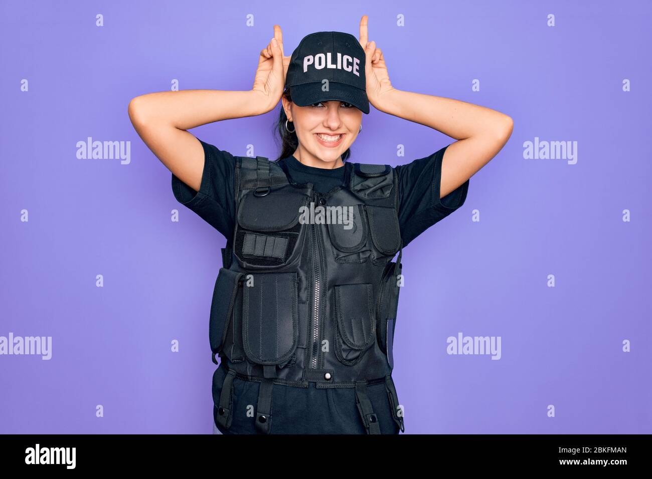 Young police woman wearing security bulletproof vest uniform over purple  background Posing funny and crazy with fingers on head as bunny ears,  smiling Stock Photo - Alamy
