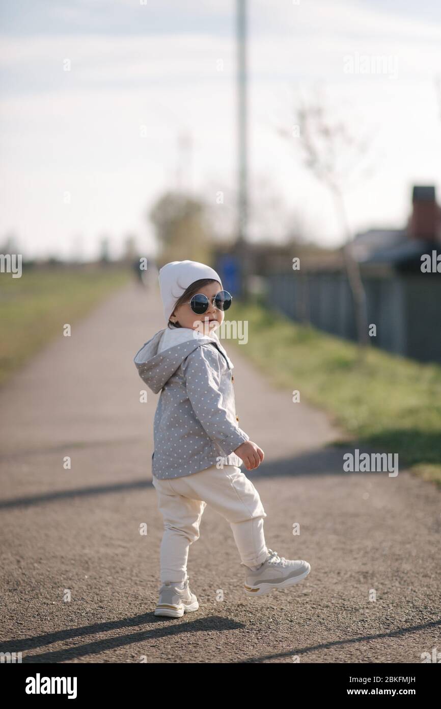 Cute baby girl walking in the park near the embankment. Stylish ...