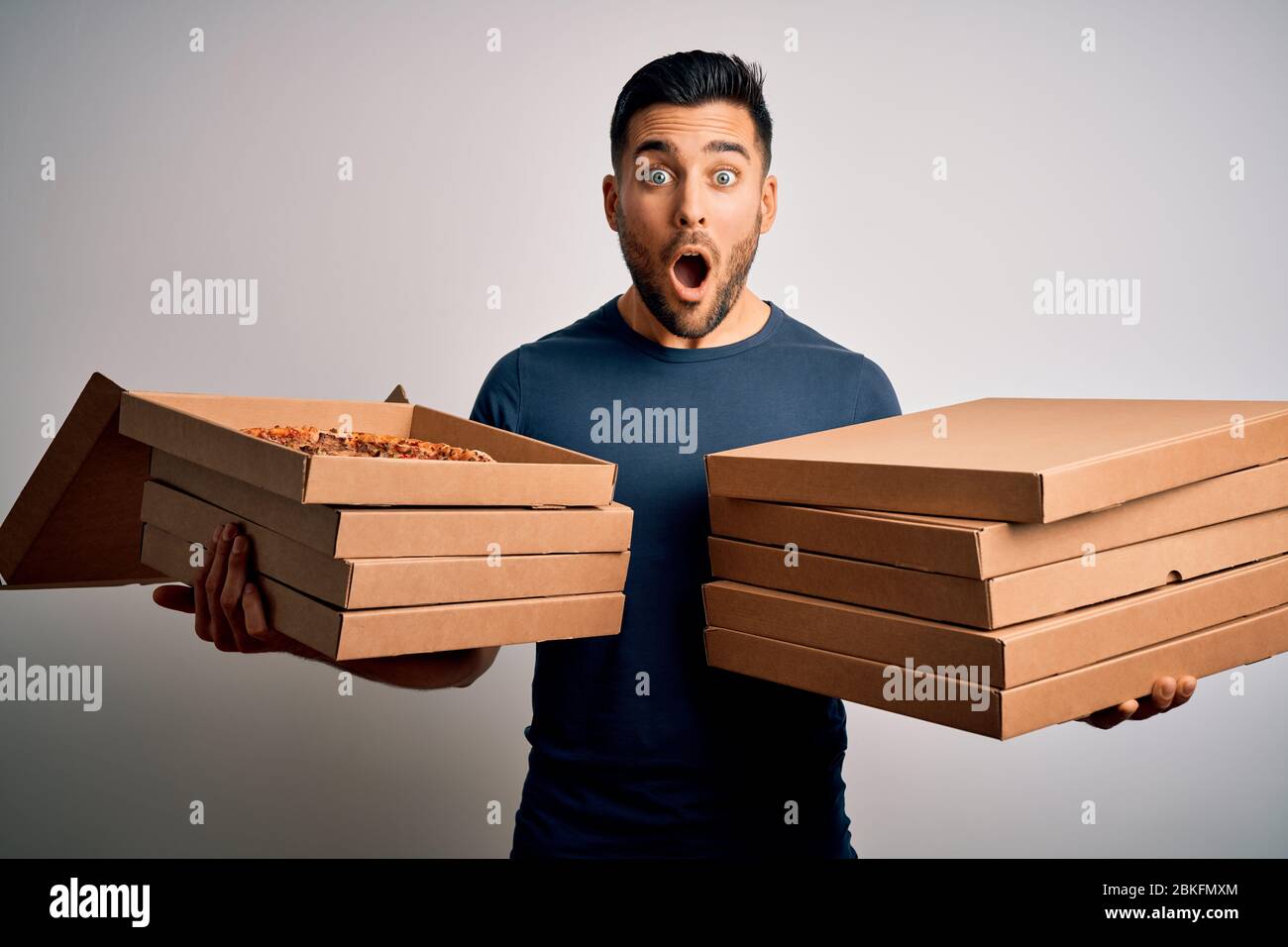 Young handsome man holding delivery boxes with Italian pizza over white