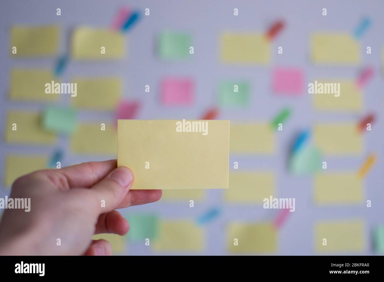 A hand holding strategy sticky note in front of a kanban board Stock ...