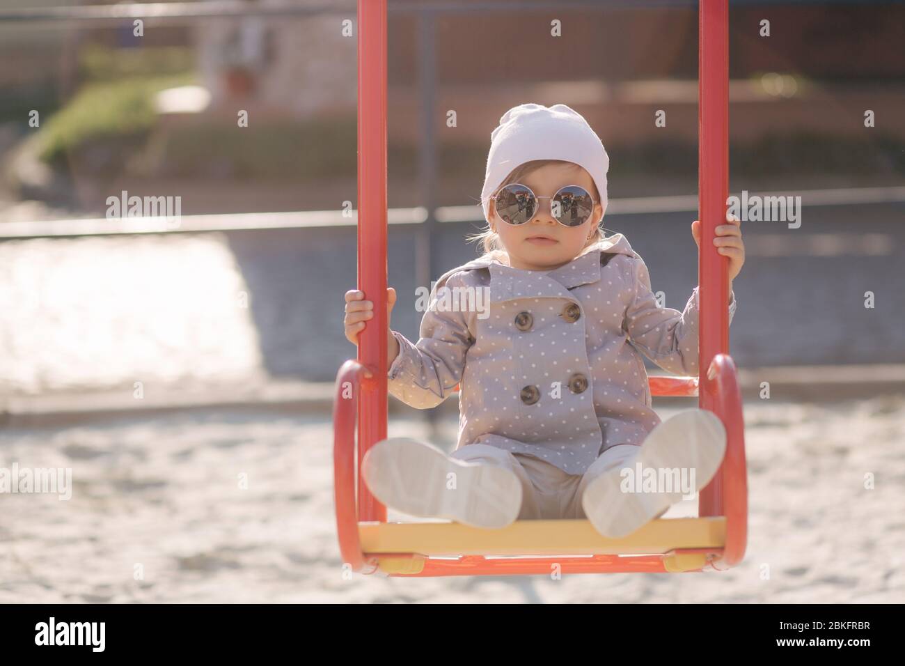 Adorable little girl on the swing set in playground. Happy little girl have fun. One and hulf year girl Stock Photo
