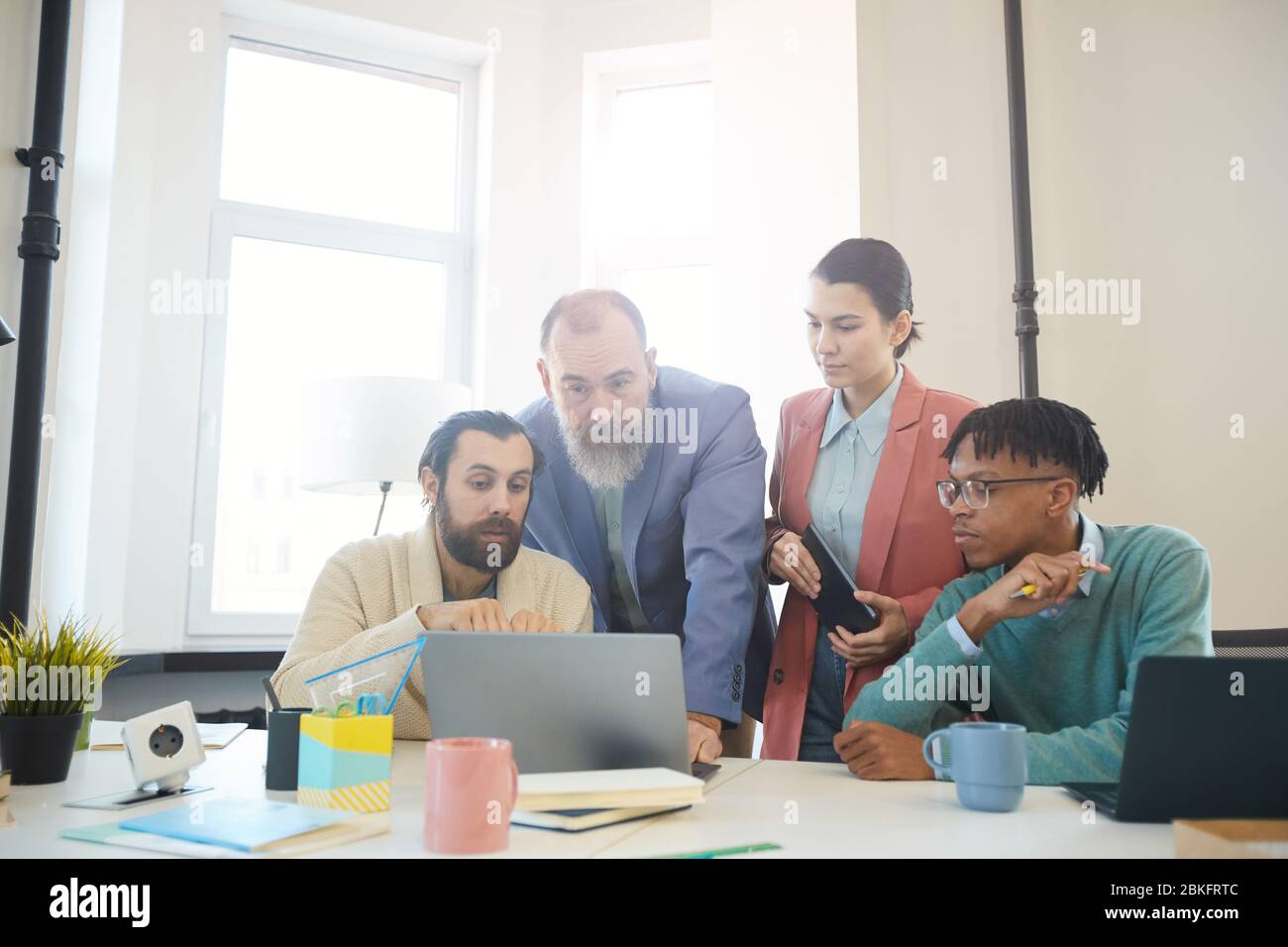 Group of four business people working together on new project looking at statistics on laptop, horizontal shot Stock Photo