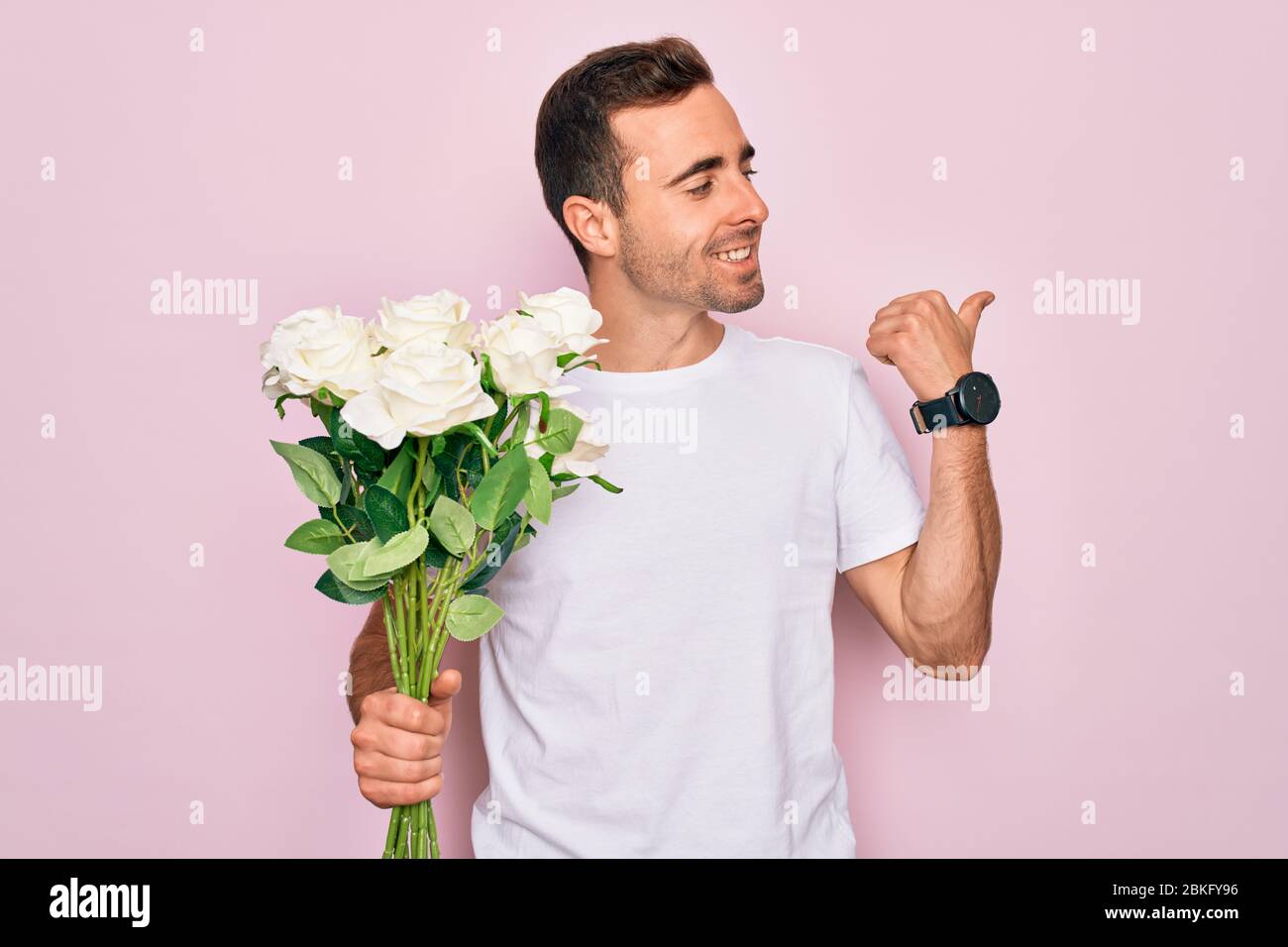 Young handsome man with blue eyes holding bouquet of flowers over pink ...