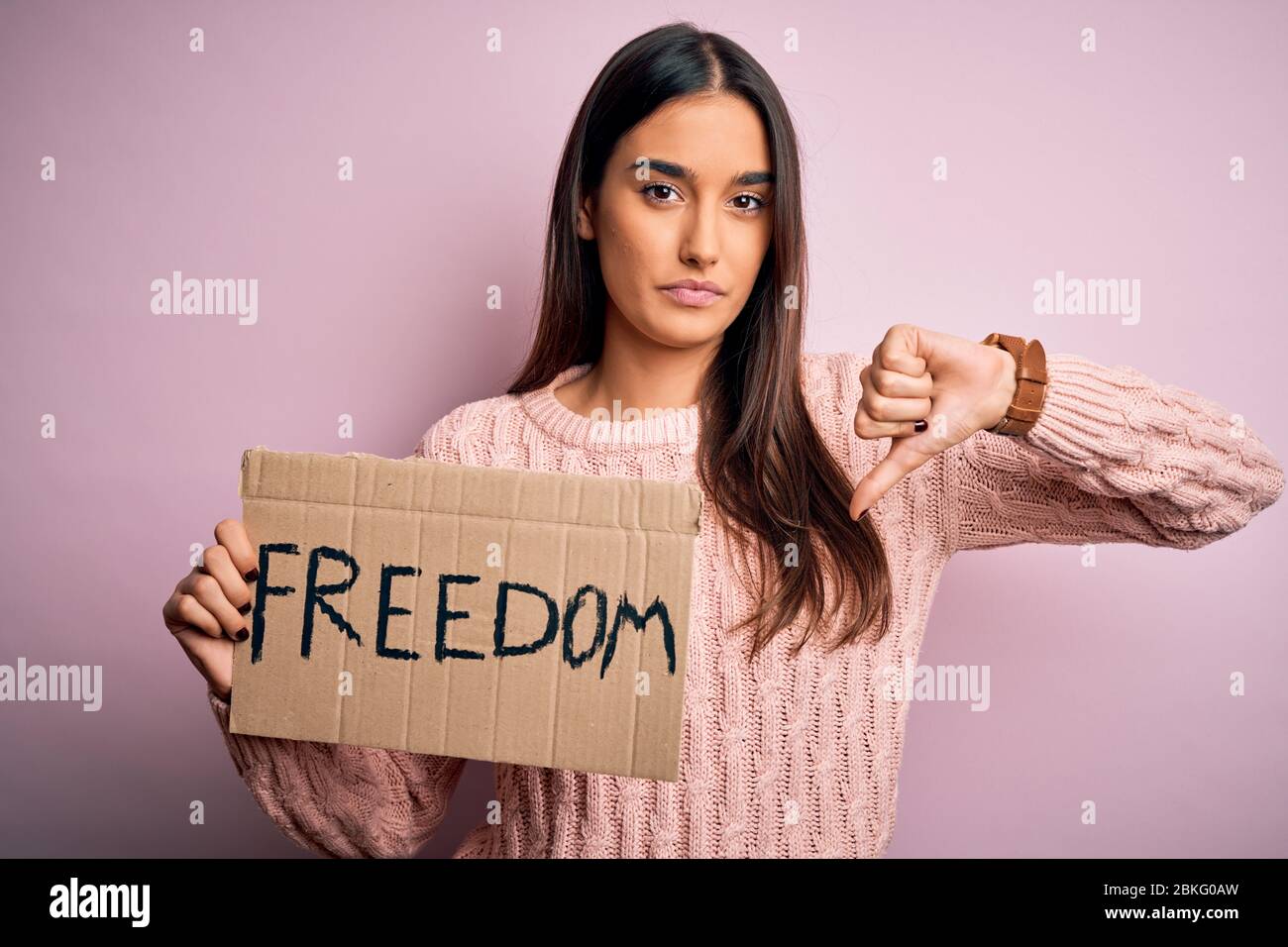 Young beautiful brunette activist woman protesting for freedom holding poster with angry face, negative sign showing dislike with thumbs down, rejecti Stock Photo