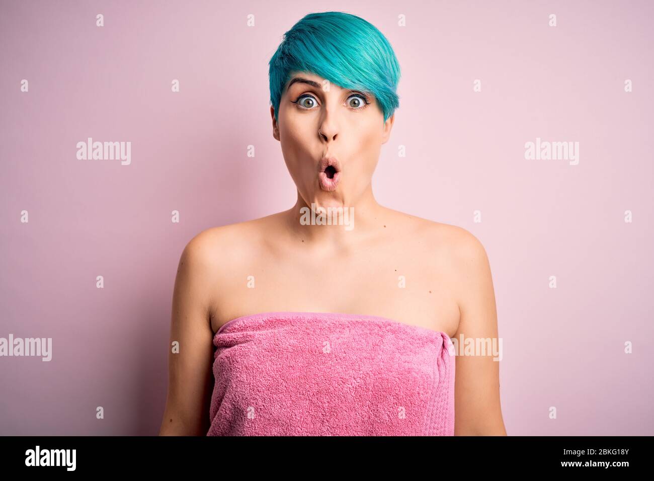 Young woman with blue fashion hair wearing towel after shower over pink ...
