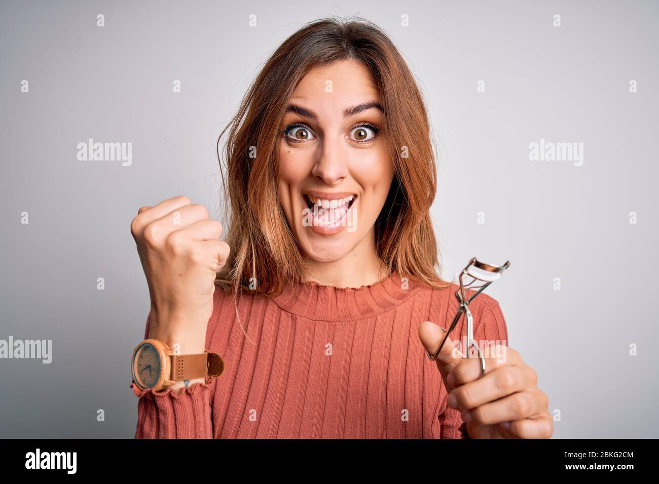 Young beautiful brunette woman using eyelash curler over isolated white ...