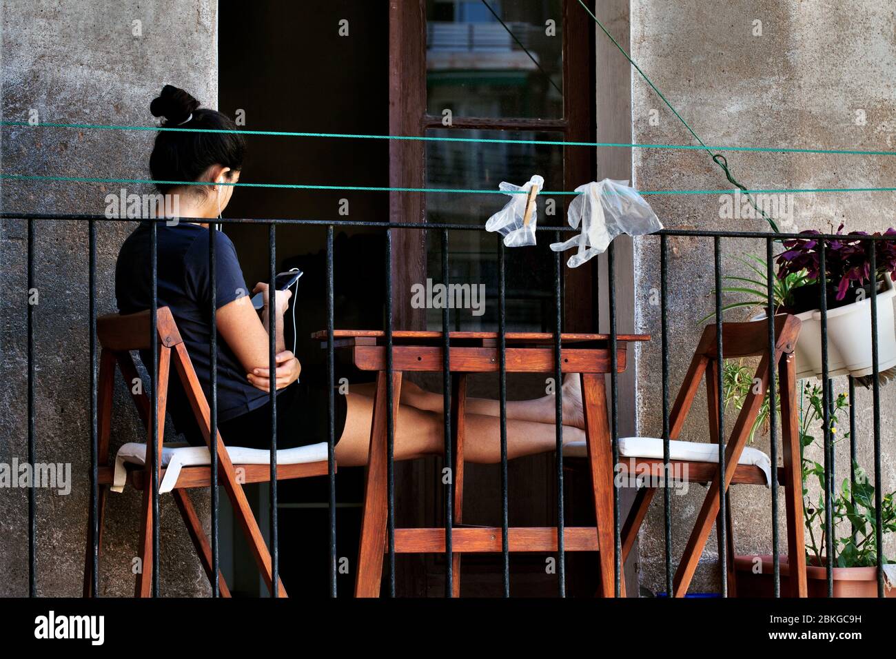 Young woman sat on her balcony using her smartphone. Stock Photo