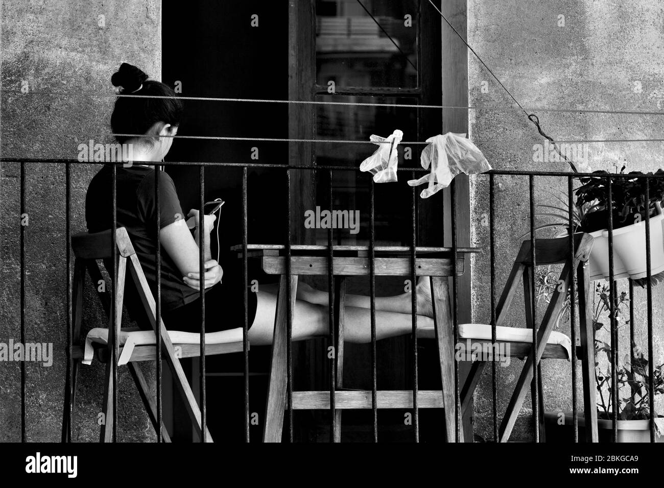 Young woman sat on her balcony using her smartphone. Stock Photo