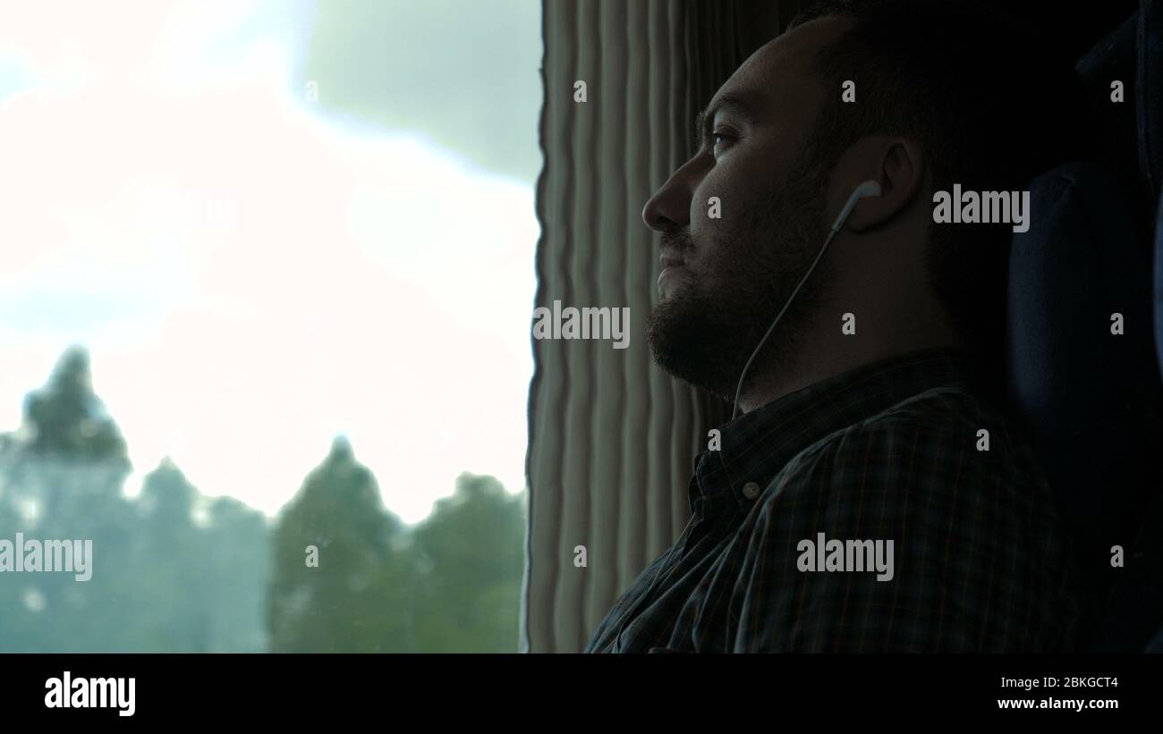 Serious man by the window on the train listening to music. Stock Photo