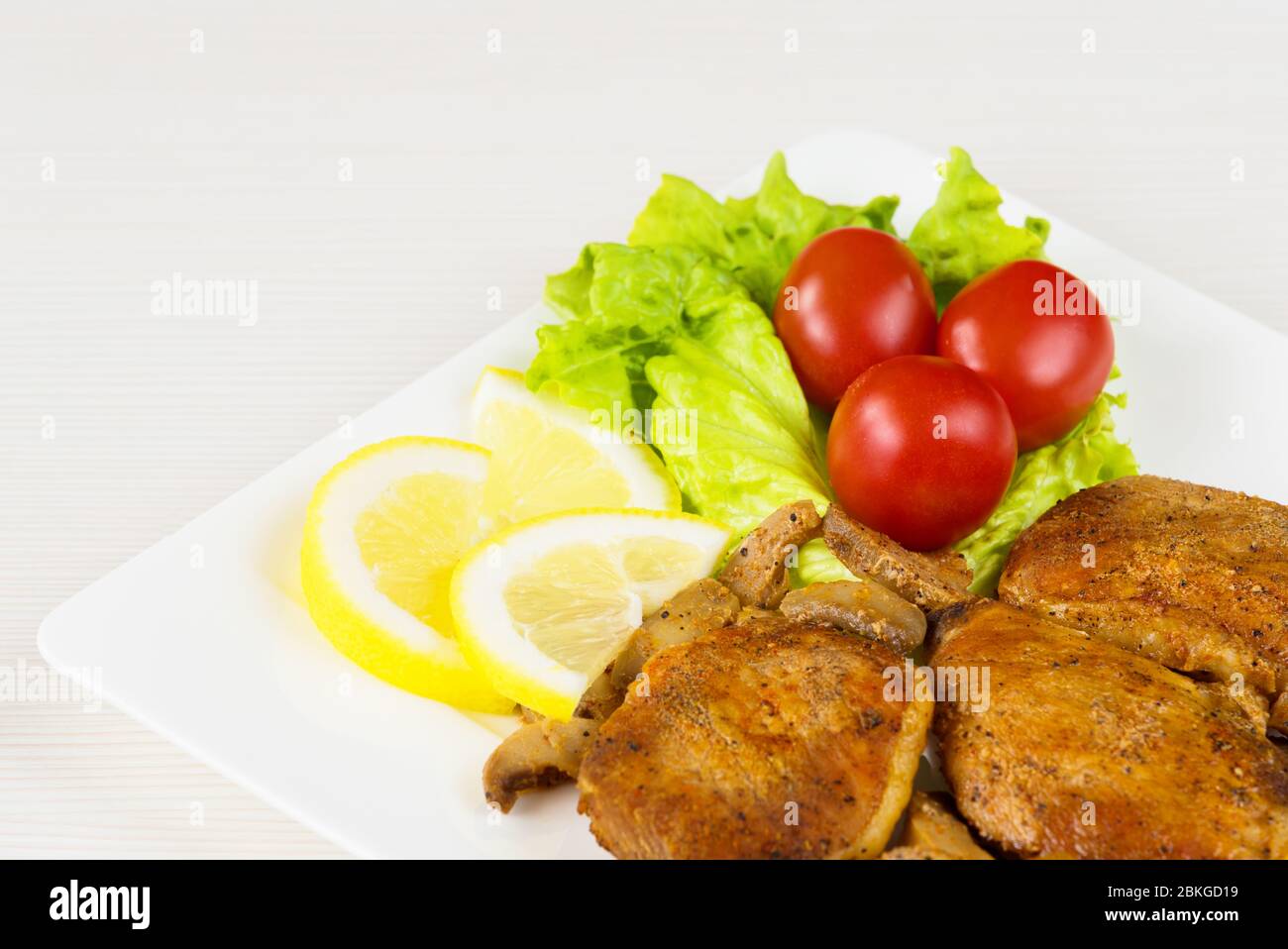 Pork fillet steak with cherry tomatoes, lemon and a lettuce in white dish on white background. Stock Photo