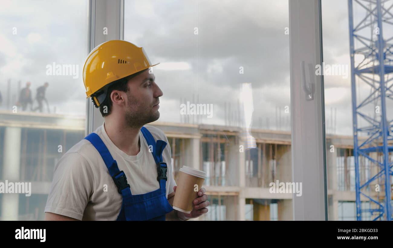 Worker wearing hardhat taking a break drinking coffee. Stock Photo