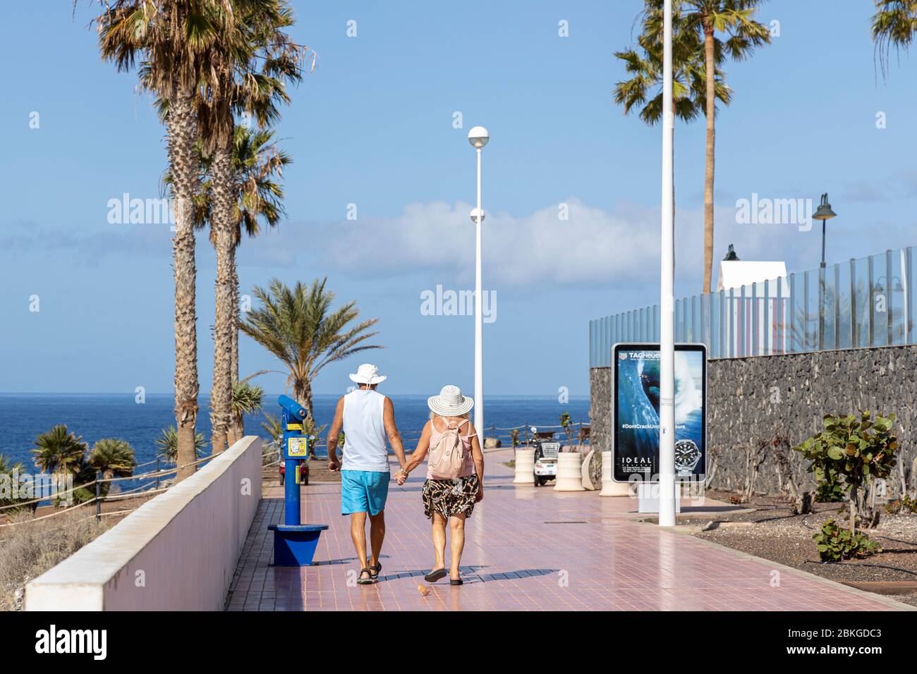 Costa Adeje, Tenerife, Canary Islands, 4 May 2020. As the Covid 19, Coronavirus state of emergency relaxes the lockdown, elderly are allowed out to exercise between the hours of 10AM and 7PM. An older couple walk hand in hand enjoying their new freedom on the promenade in Fanabe. Stock Photo