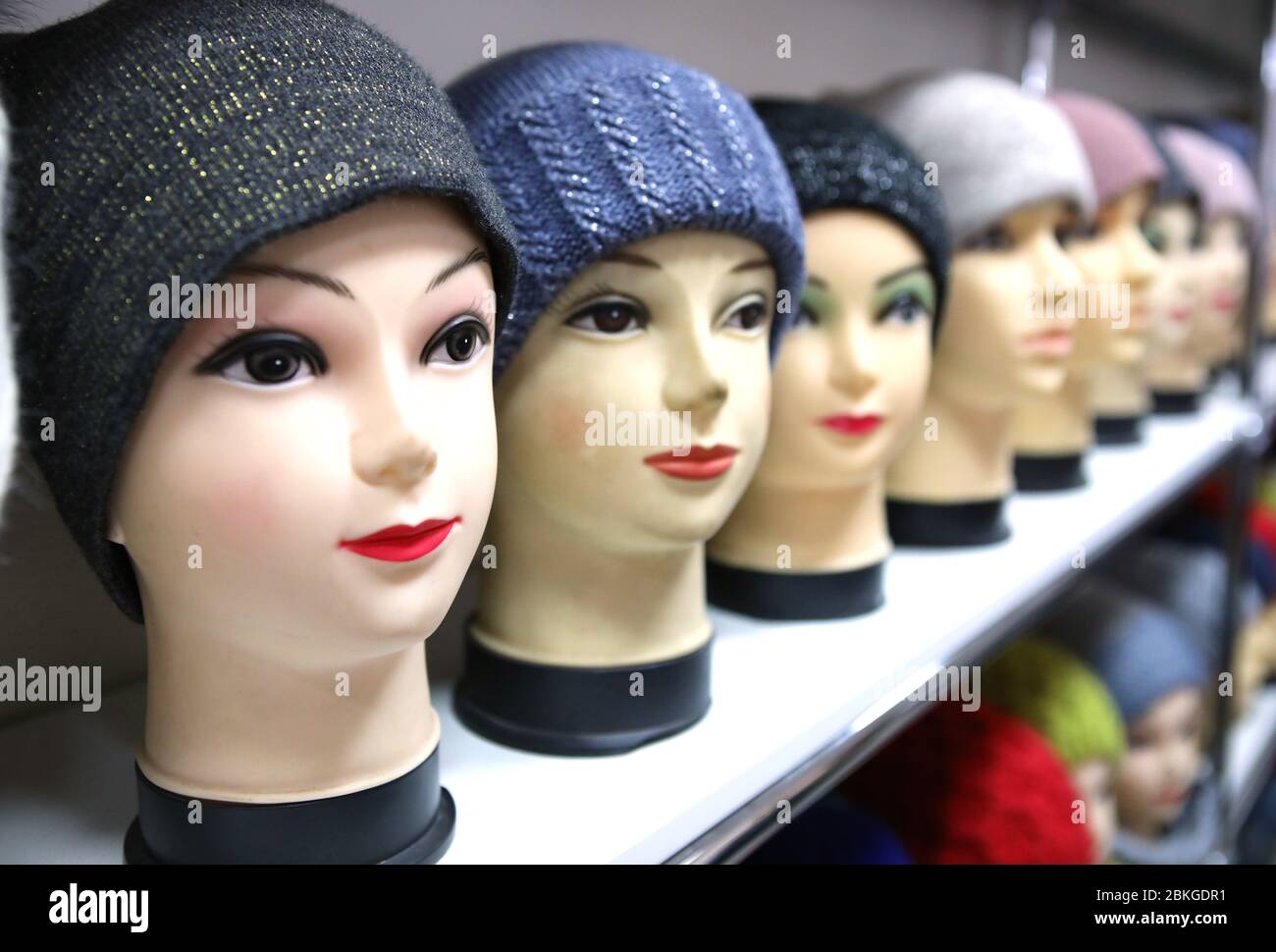 Mannequin heads in knitted hats and scarves. Mannequins female heads in hats and scarfs close up. Woolen knitted caps and scarves. Female headdresses. Stock Photo