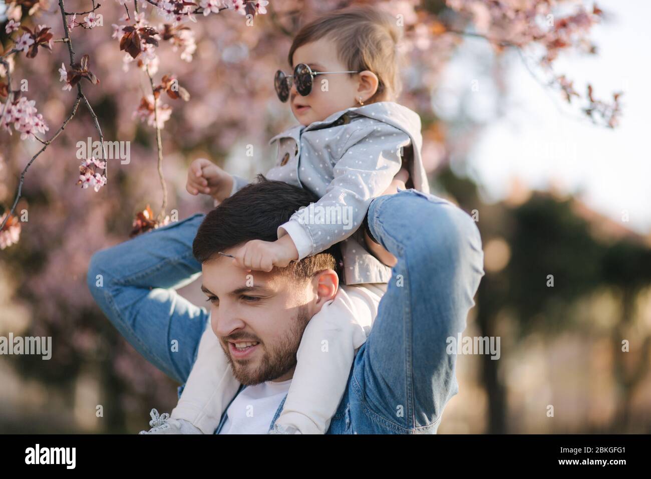 Adorable little daughter sitting on dad's neck and smels pink flowers