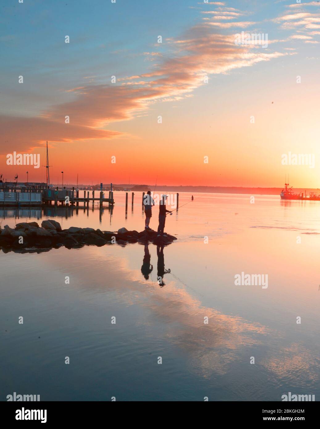 Two young men fishng of the landing at Westport harbor as the sun sets May 3 2020 , Westport Ma USA  photo by bill belknap Stock Photo