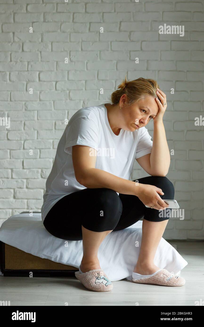 Upset stressed woman holding cellphone disgusted with message she received home background. Sad looking human face expression emotion feeling reaction Stock Photo