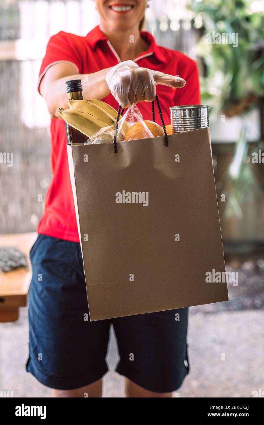 Delivery woman in protective gloves delivers paper bag with food ...