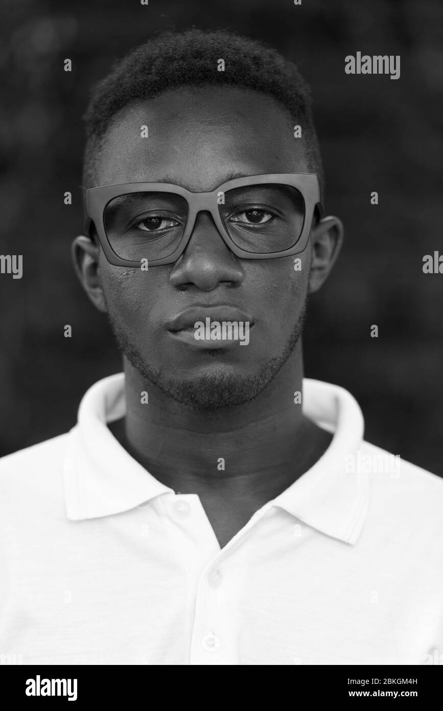 Face of young African nerd man wearing eyeglasses outdoors in black and white Stock Photo