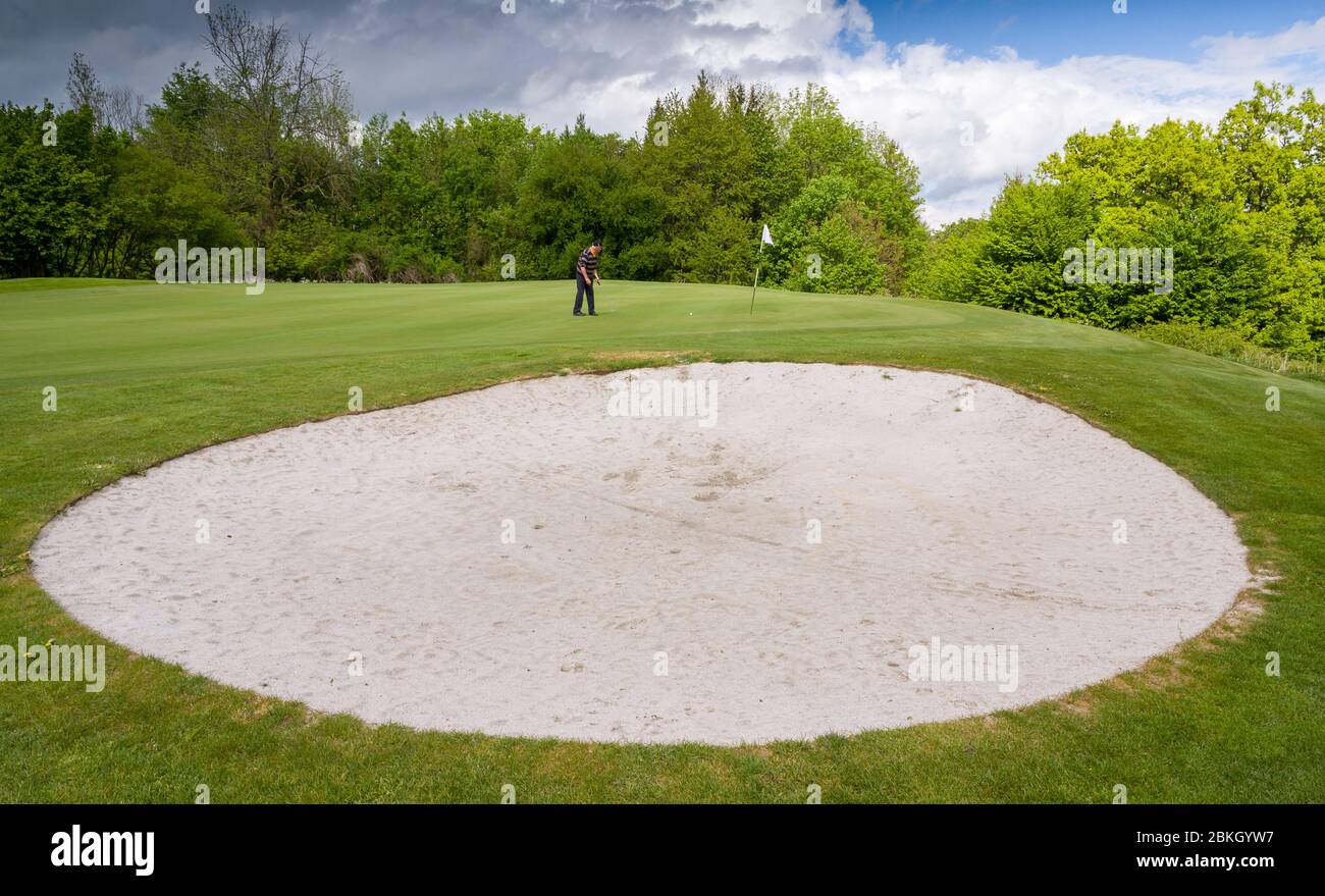 Wolfratshausen, Germany. 04th May, 2020. A member of the Bergkramerhof Golf  Club puts his golf ball above a sand bunker. The golf course opened during  the Corona crisis despite the ban. Credit: