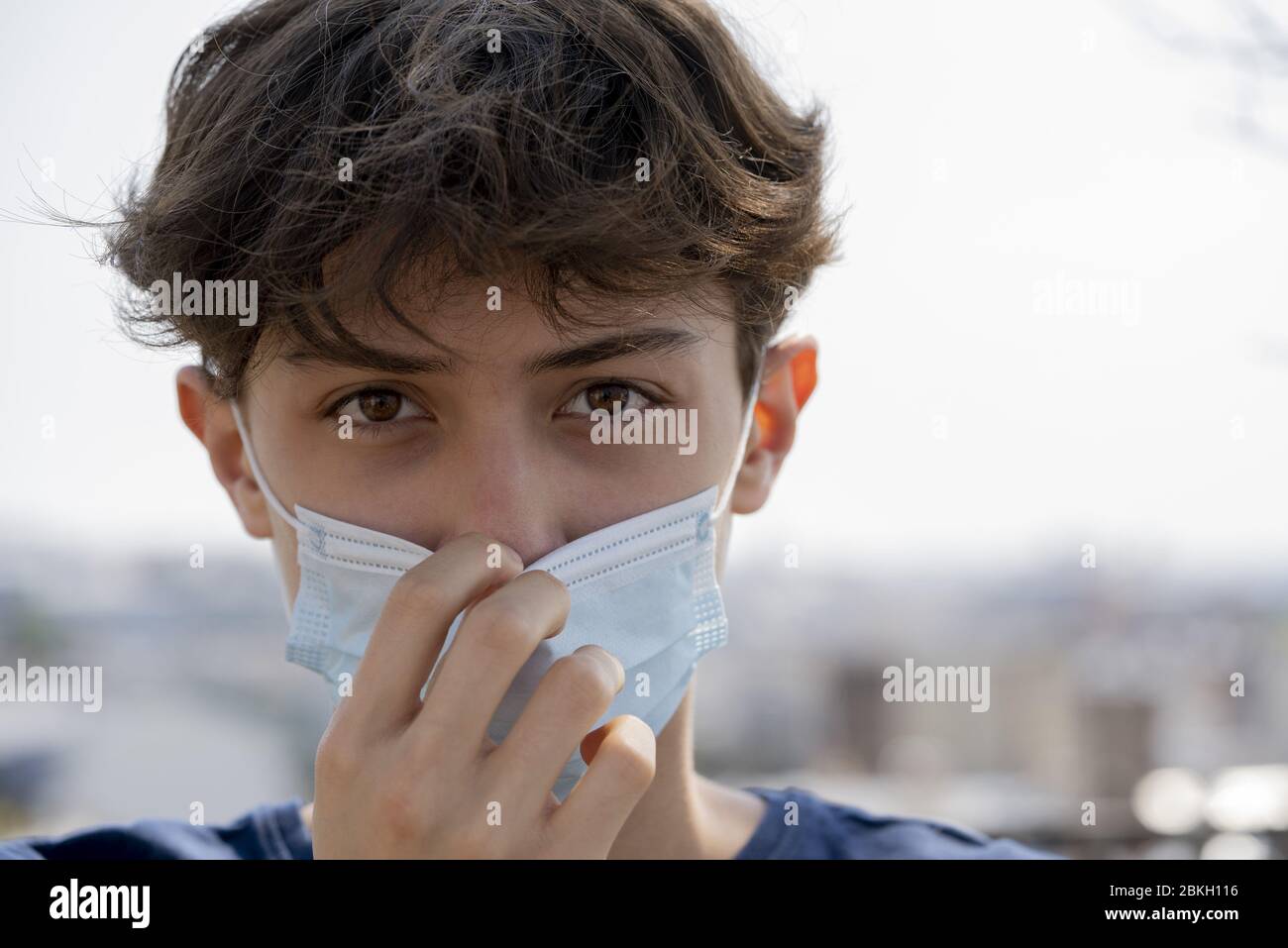 Close up of teenage boy wearing blue surgical mask outdoors Stock Photo