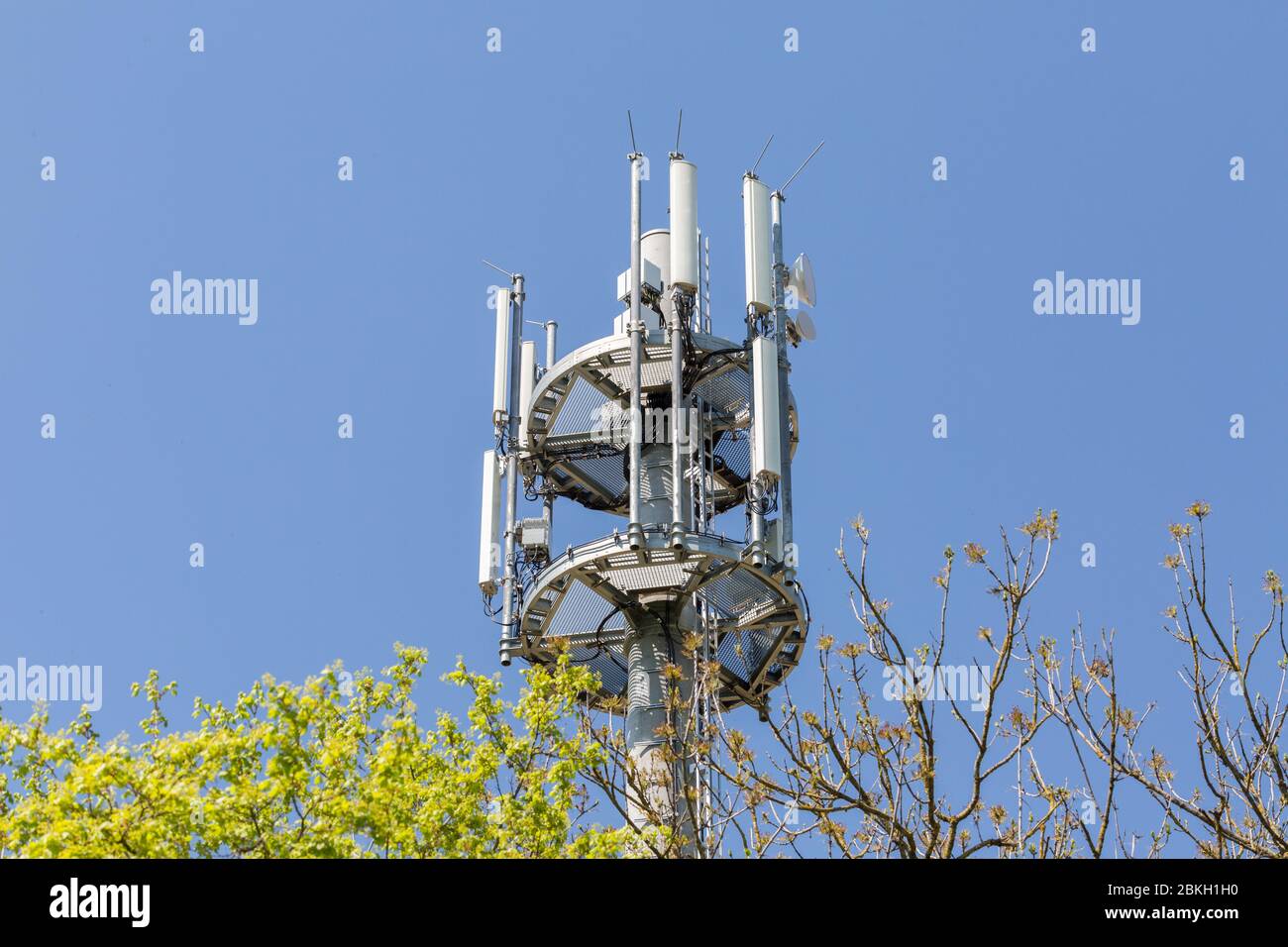 View on the top part of a mobile phone / telecommunications mast. Used for transmitting signals and data. E. g. for 5G networks. Blue sky background. Stock Photo