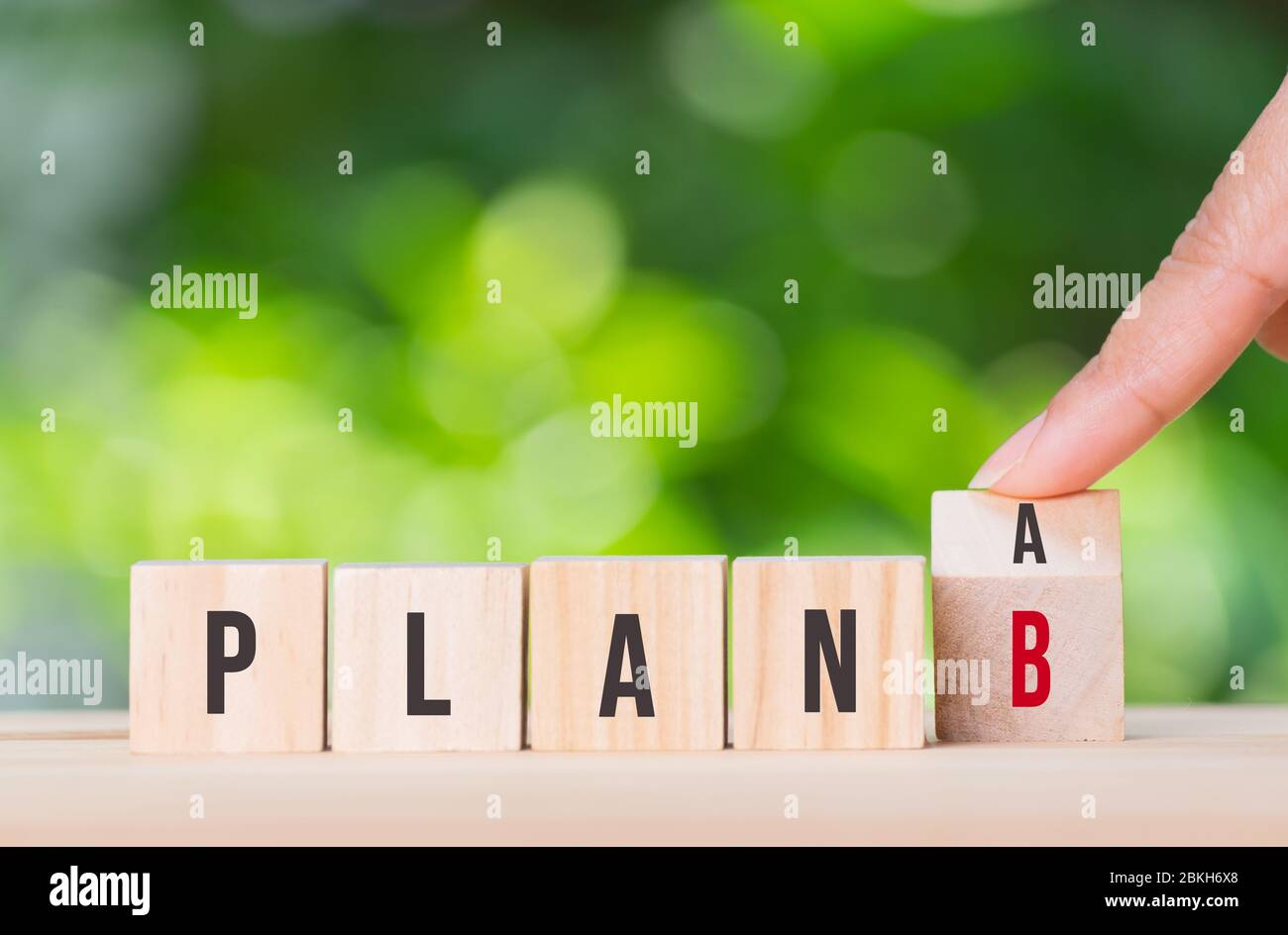 Hand flip wooden cube with the word PLAN A to PLAN B over green bokeh  background. Business plan concept. Covid-19 crisis. Copy space for advertisers. Stock Photo