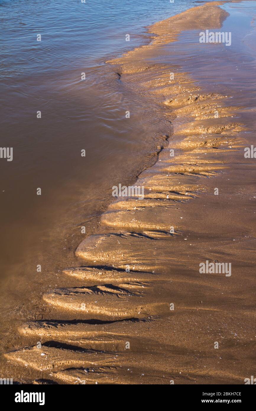 View on a wave from a sand on a beach after a high tide. Structured wavy line, enlightened by a late afternoon sunlight. Essaouira, Morocco. Stock Photo