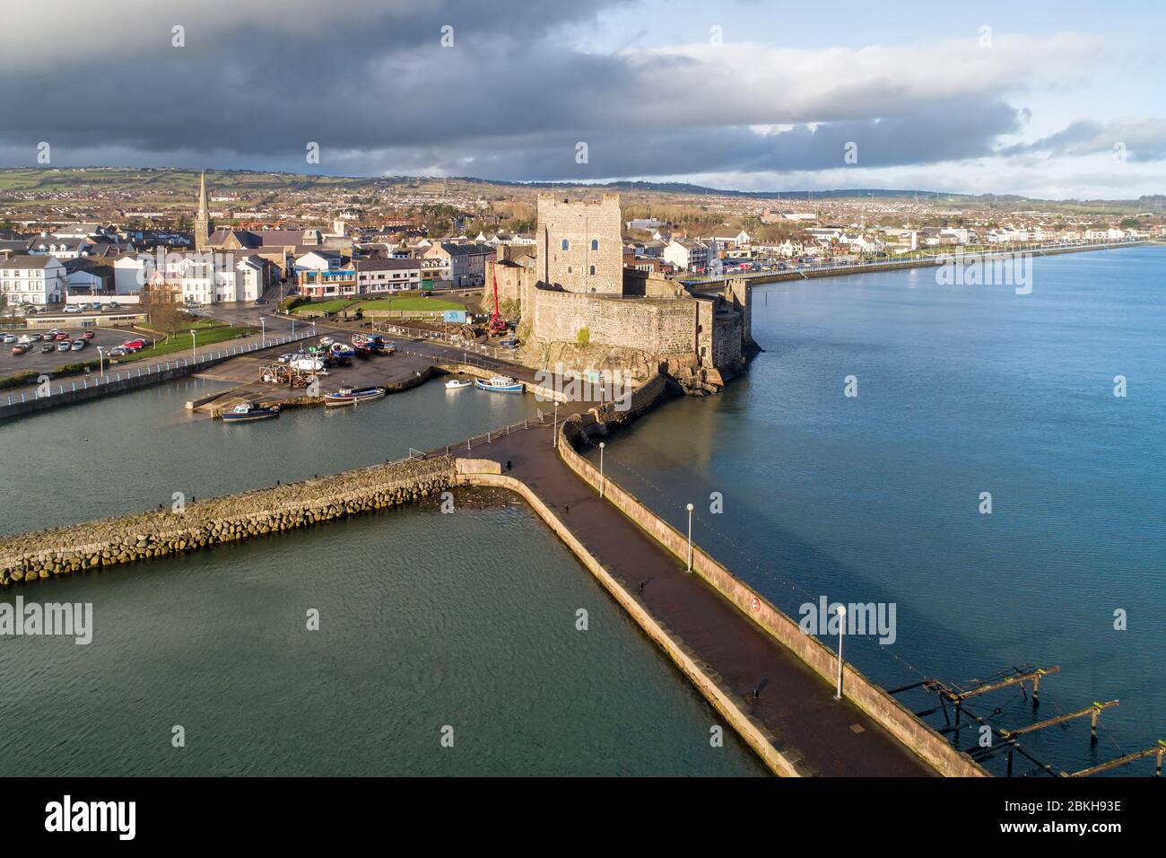 Medieval Norman Castle, harbor with boat ramp and wave breaker in Carrickfergus near Belfast, Northern Ireland, UK. Aerial view in sunset light Stock Photo