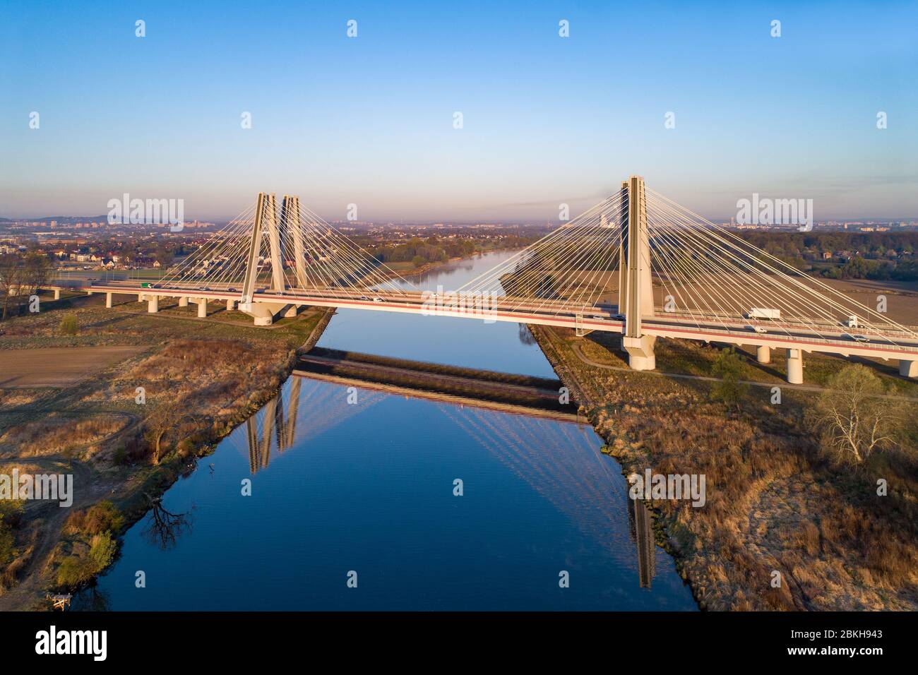 New modern double cable-stayed bridge with wide three-lane roads over Vistula River in Krakow, Poland, and its reflection in water at sunrise. Stock Photo