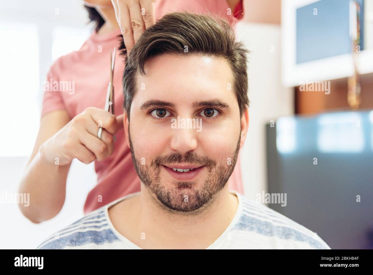 Woman cutting the hair of a young man in a makeshift hairdresser's at home. Quarantine Concept. Stock Photo