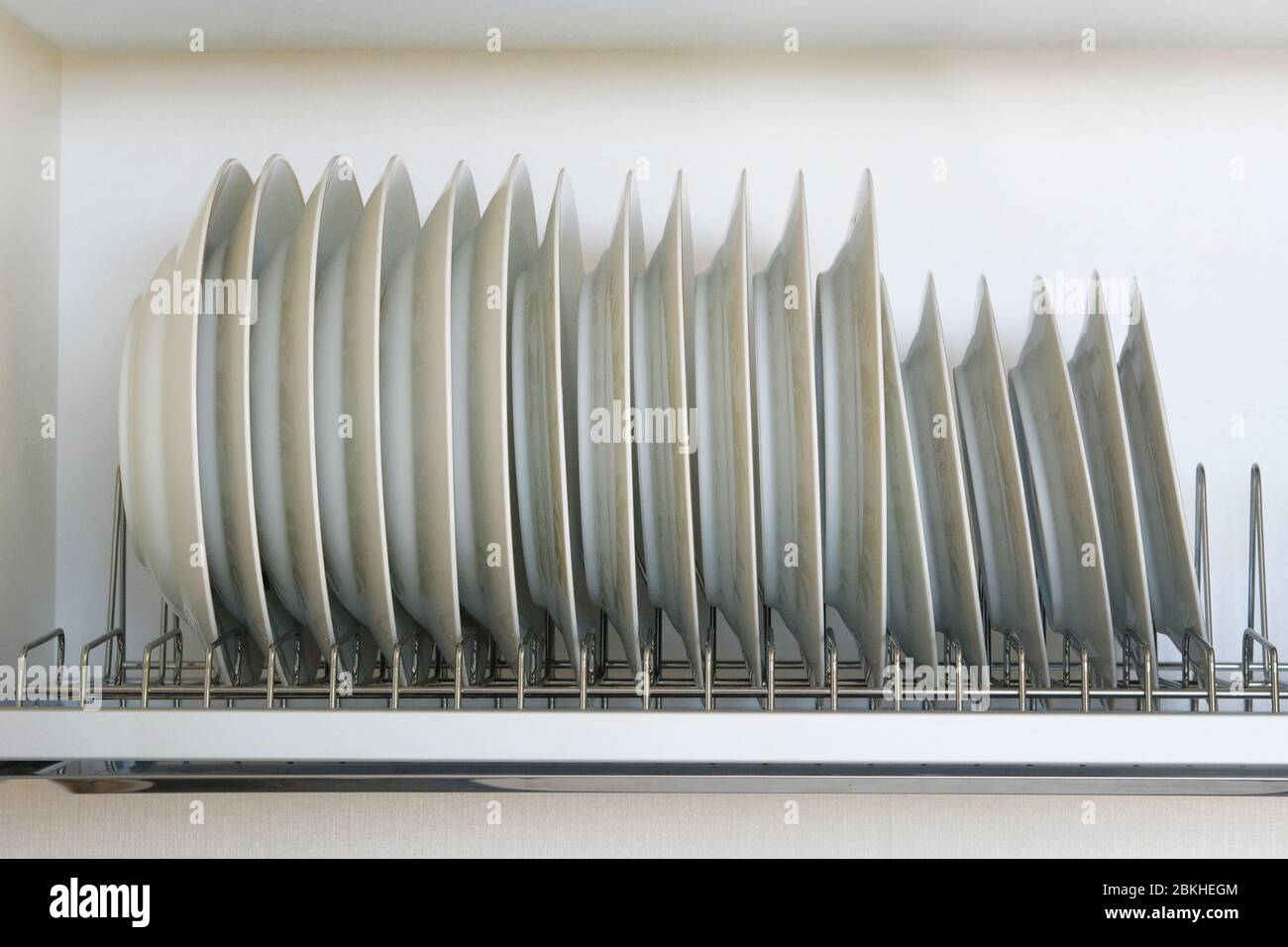 Shelf for tableware drying in modern kitchen. White glass and ceramic dishes on metal rack inside kitchen cupboard. Stock Photo
