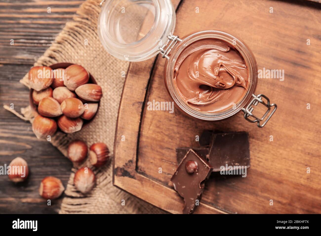 Jar with tasty chocolate paste and hazelnuts on table Stock Photo