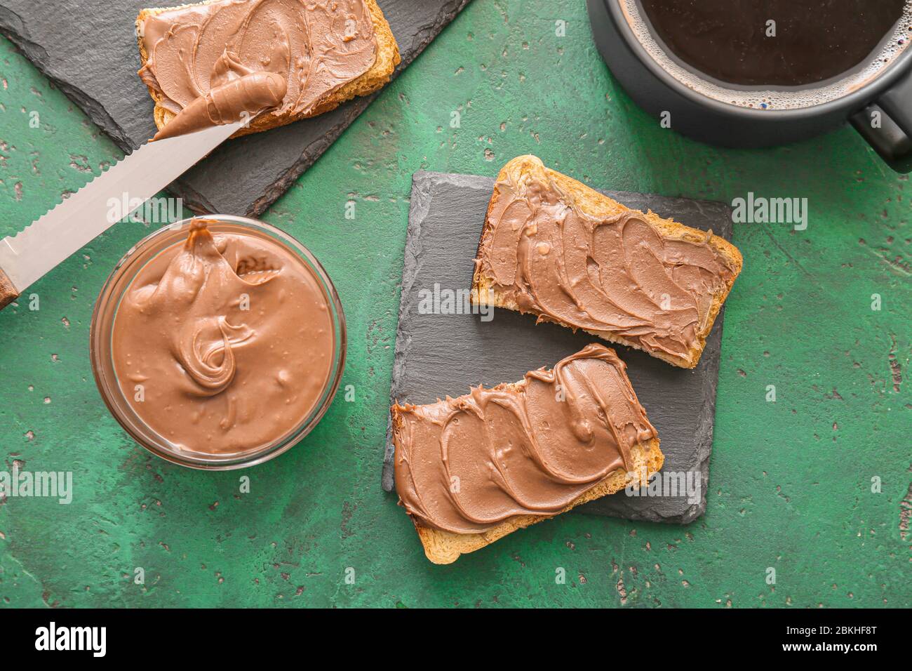 Fresh bread with chocolate paste and cup of coffee on color background ...