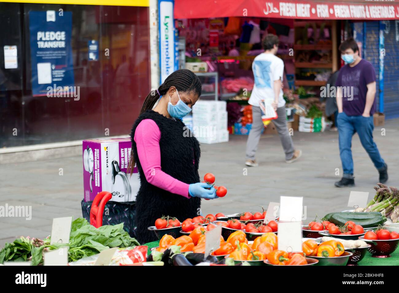 Stall-holder in Lewisham Market, wearing a Face Mask and inspecting her tomatoes, during the COVID-19 Pandemic, Lewisham High Street Stock Photo