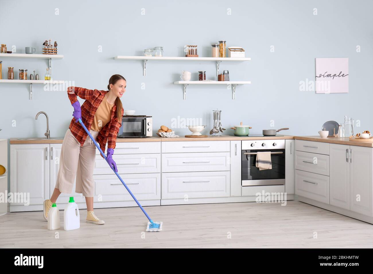 Young woman mopping floor in kitchen Stock Photo