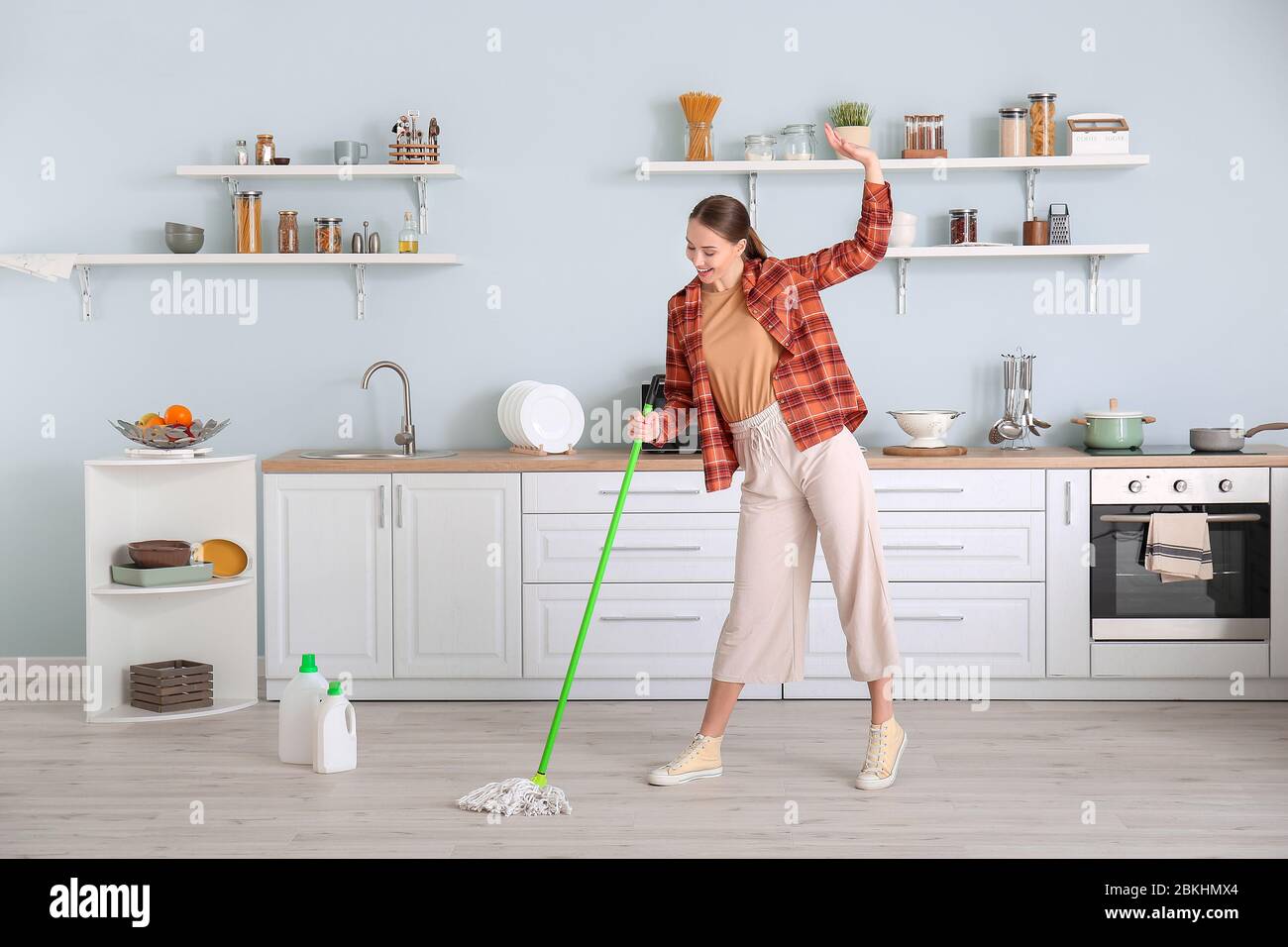 Young woman having fun while mopping floor in kitchen Stock Photo