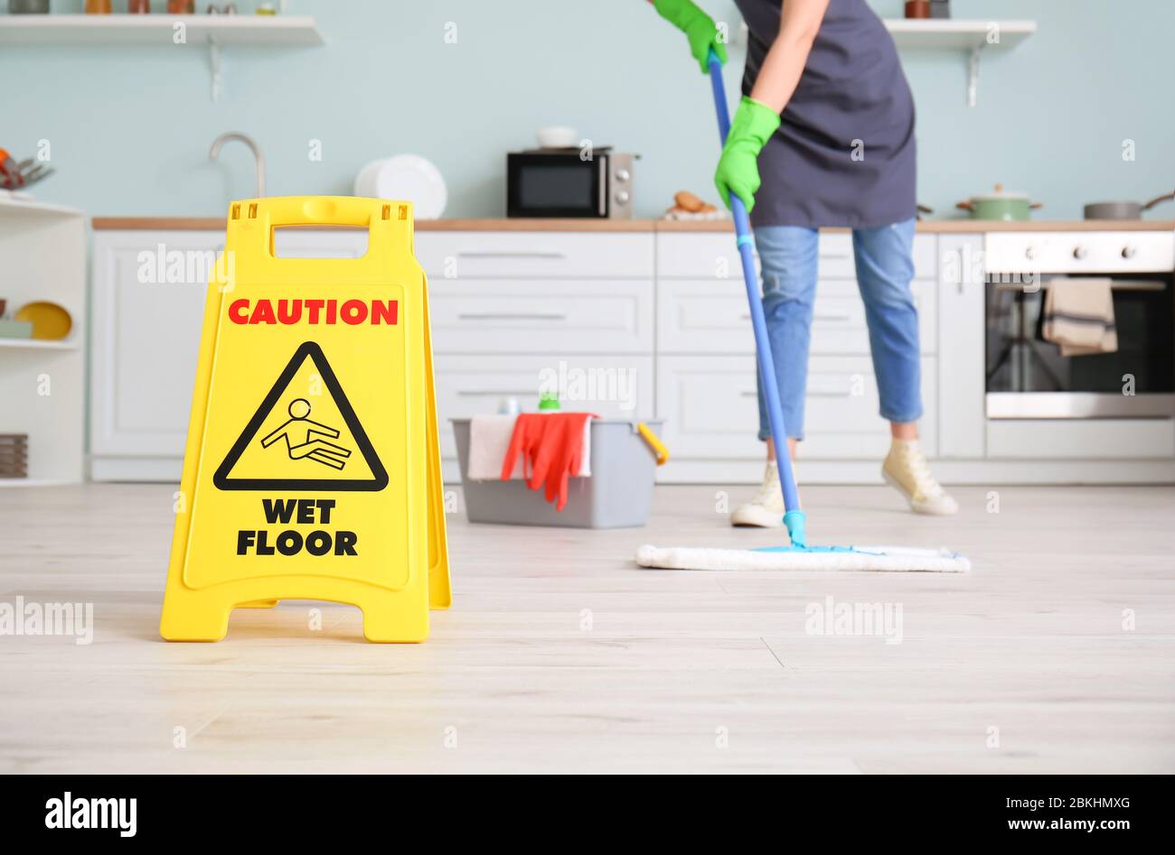 Young woman mopping floor in kitchen Stock Photo