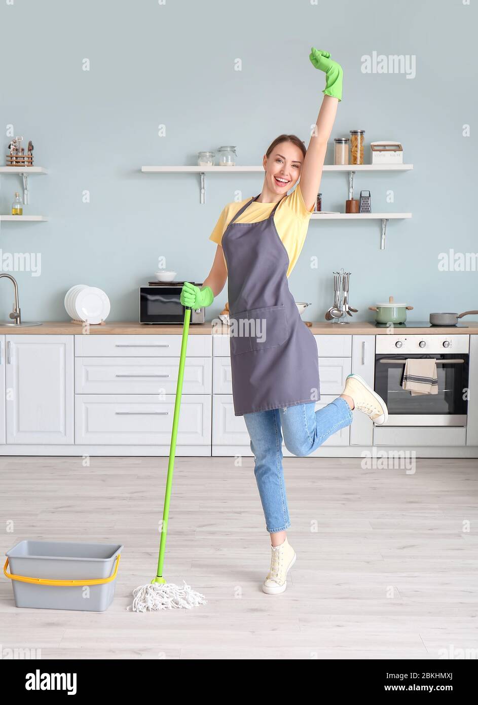 Young woman having fun while mopping floor in kitchen Stock Photo