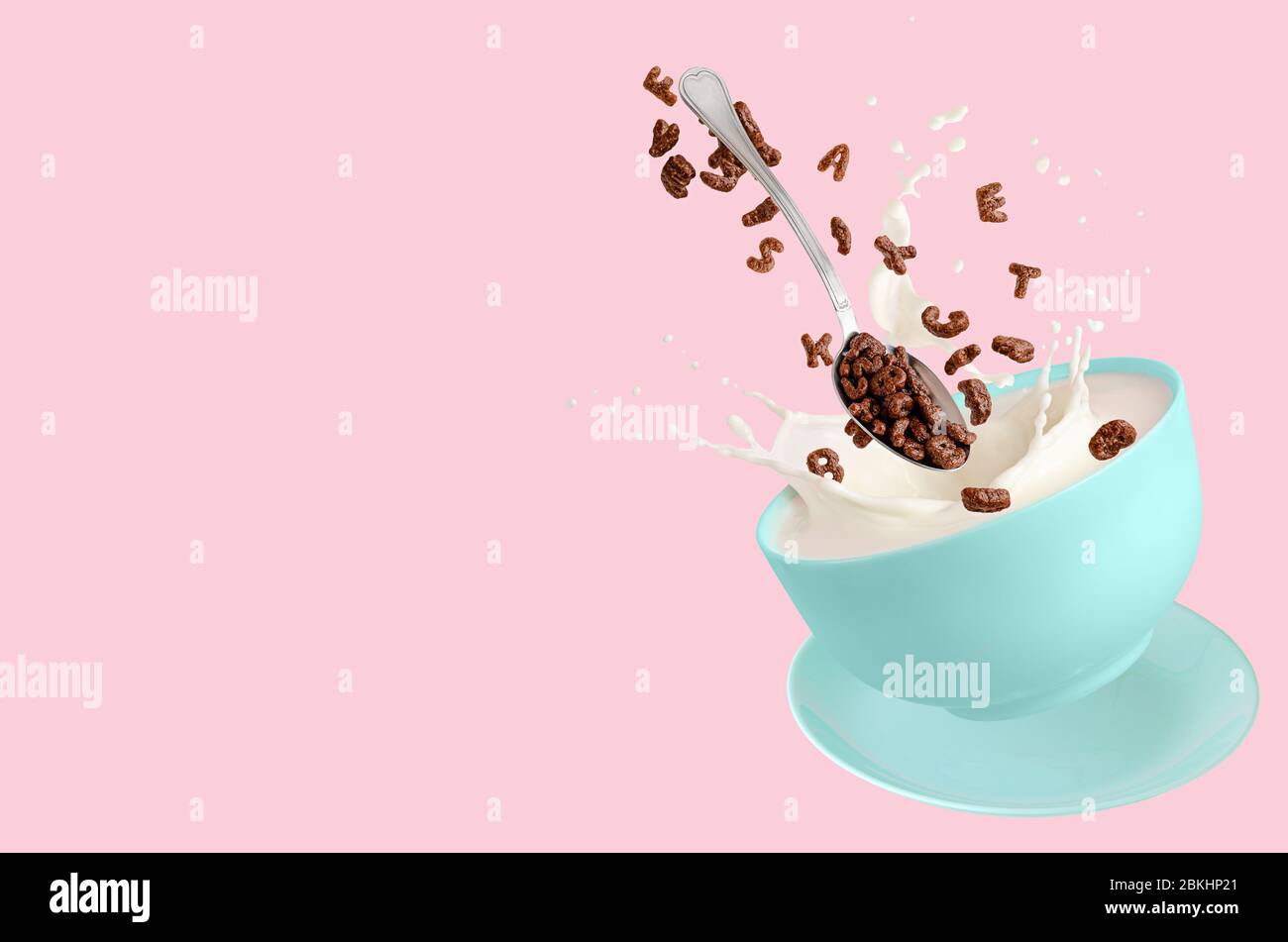 Cereal cocoa letters falling into blue bowl with splashing milk on pink background. Dry breakfast for children. Copy space. Stock Photo