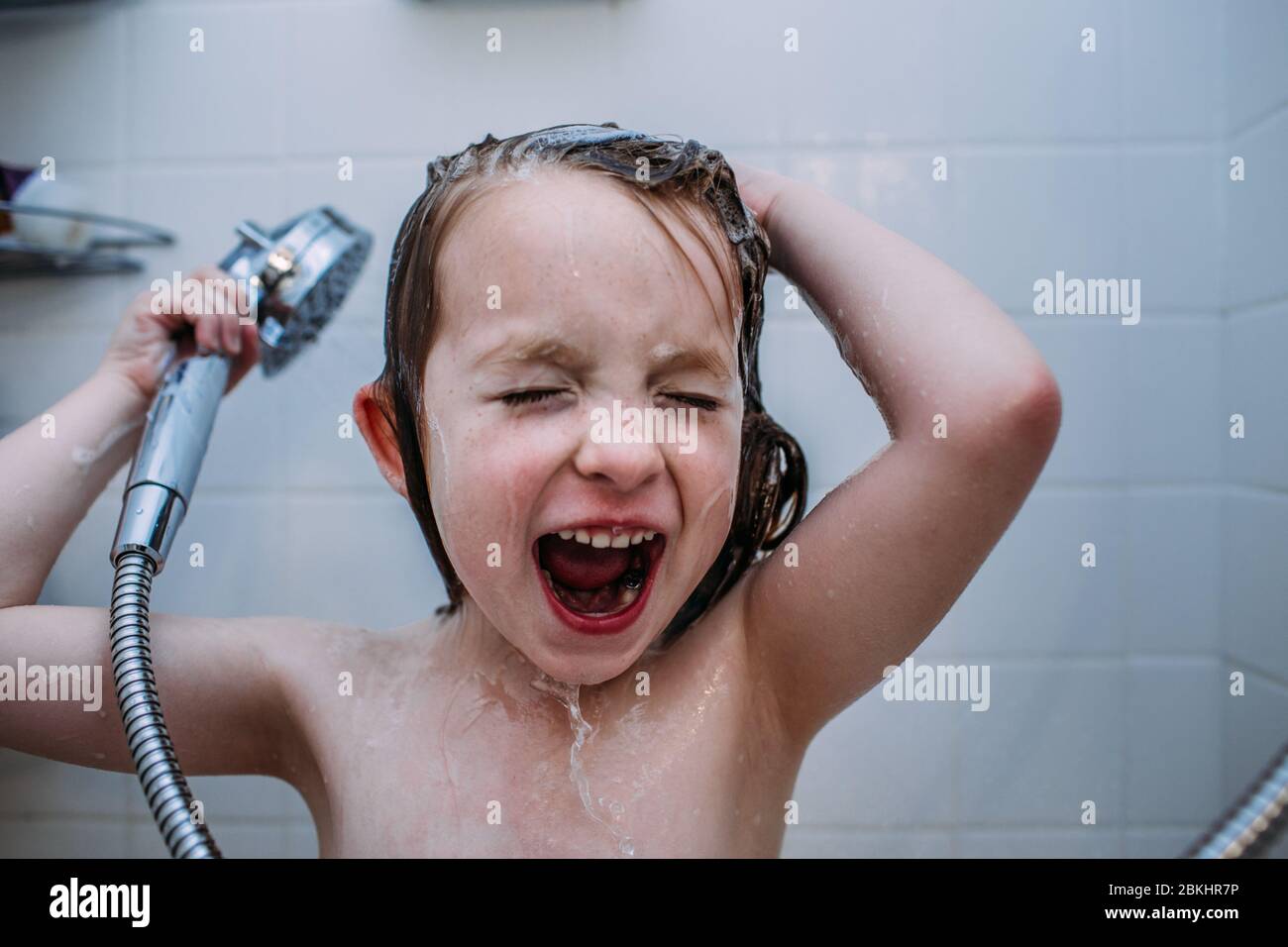 close up of young child singing in shower while washing hair Stock