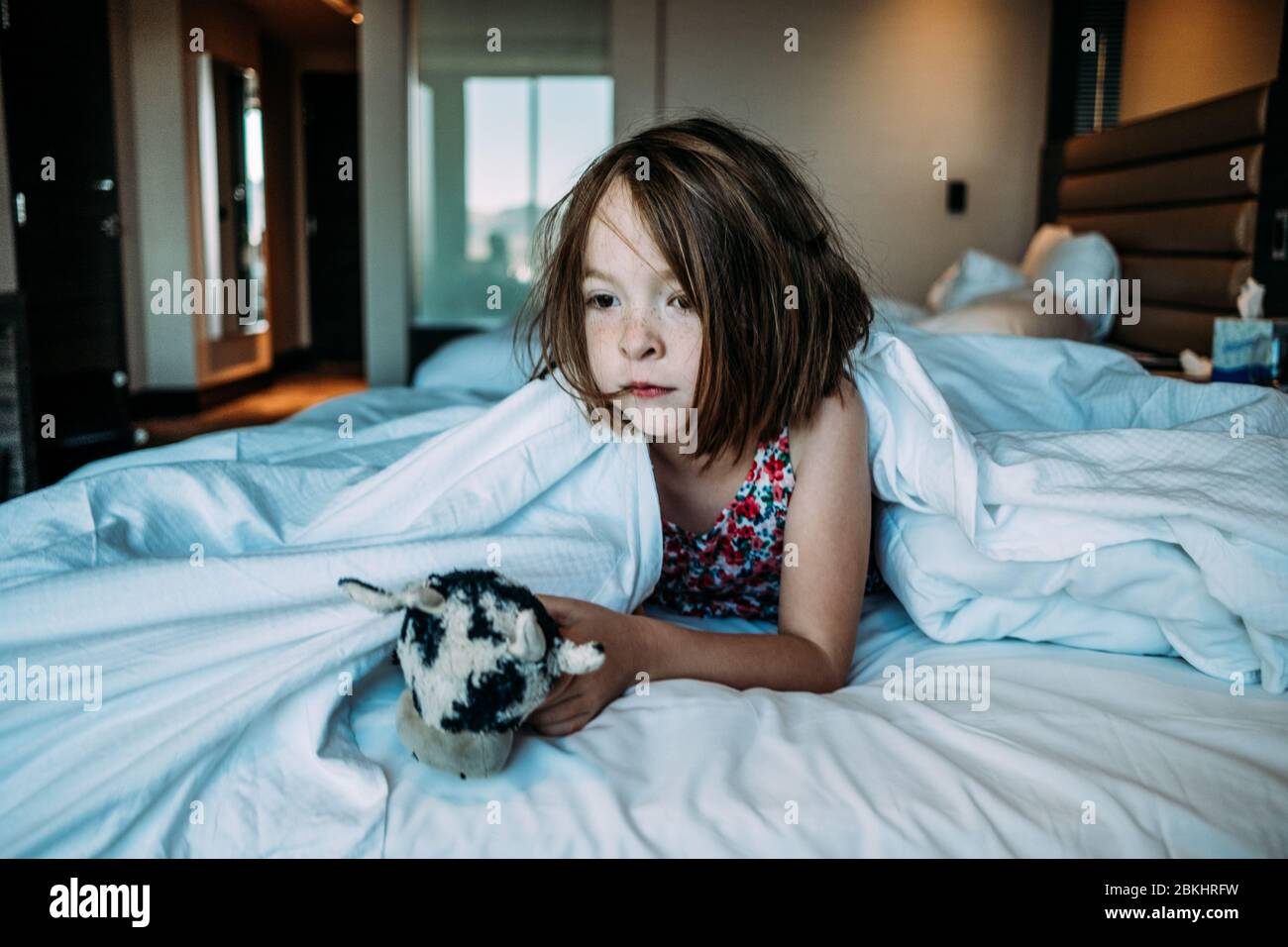 young girl in hotel bed waking up from a nap with her toy Stock Photo