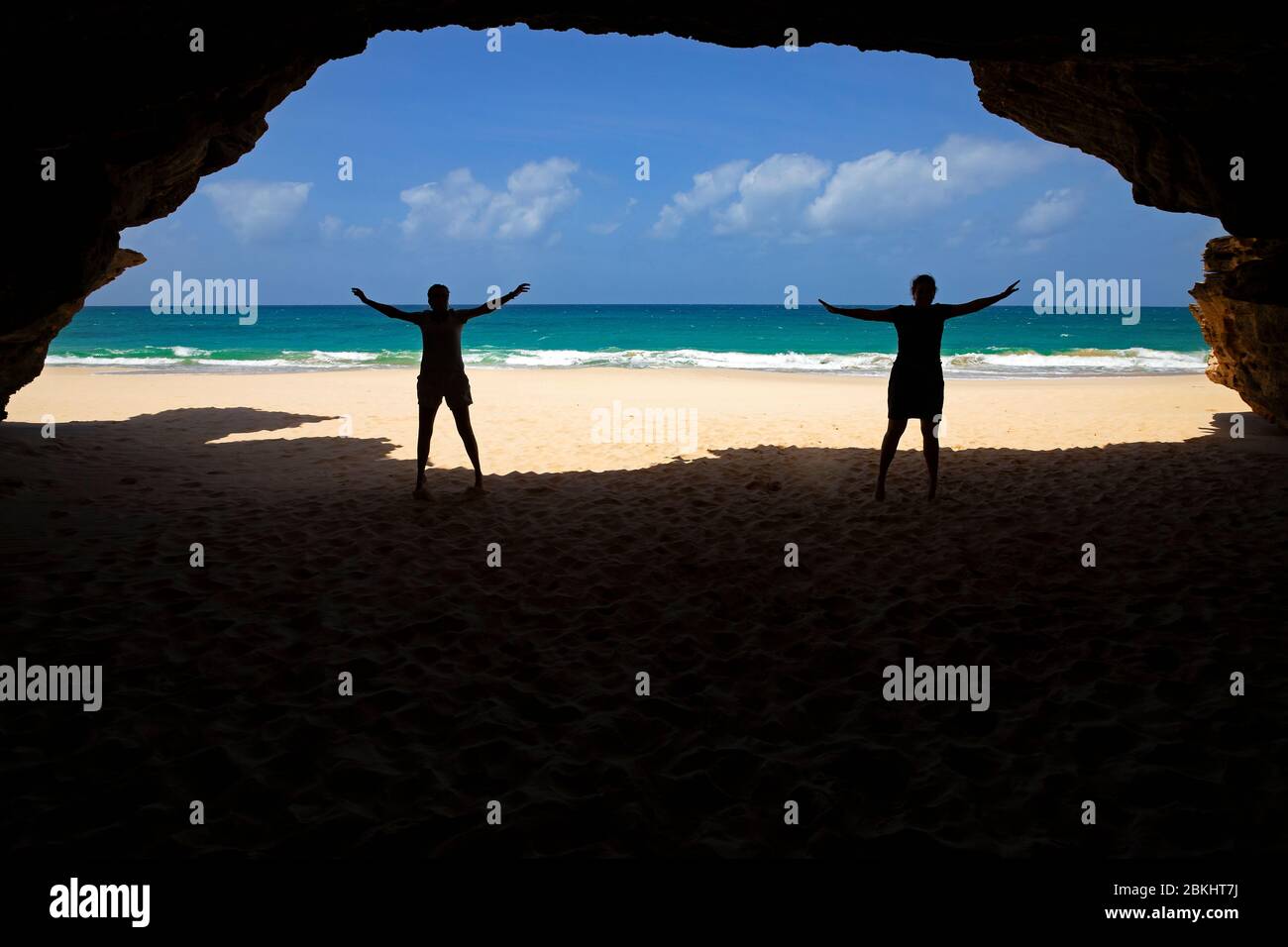 Two tourists silhouetted at entrance of sea cave at Praia de Santa Mónica, sandy beach on the island of Boa Vista, Cape Verde / Cabo Verde Stock Photo